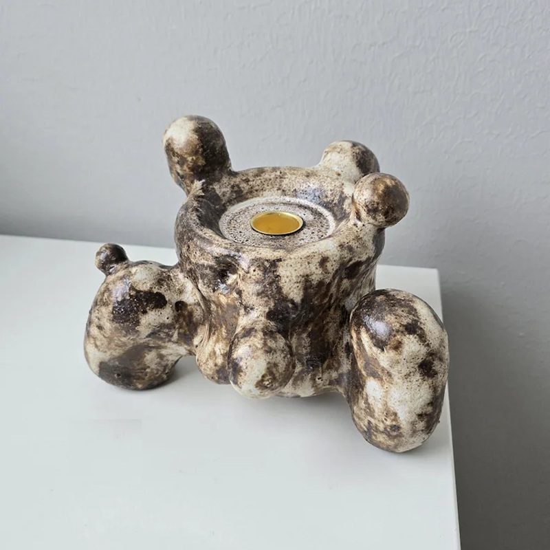 Close-up of single organic bubble ceramic candle holder (mottled glaze texture) on light table, against gray wall